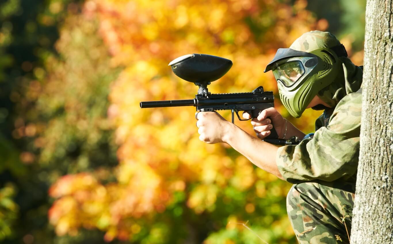 gracz paintballa celujący zza drzewa