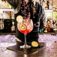 barman przygotowuje kolorowego drinka z limonką i marakują