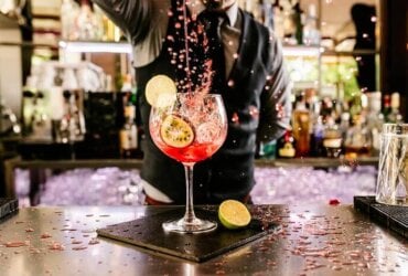 barman przygotowuje kolorowego drinka z limonką i marakują