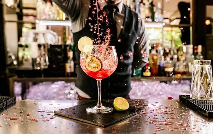 barman przygotowuje kolorowego drinka z limonką i marakują