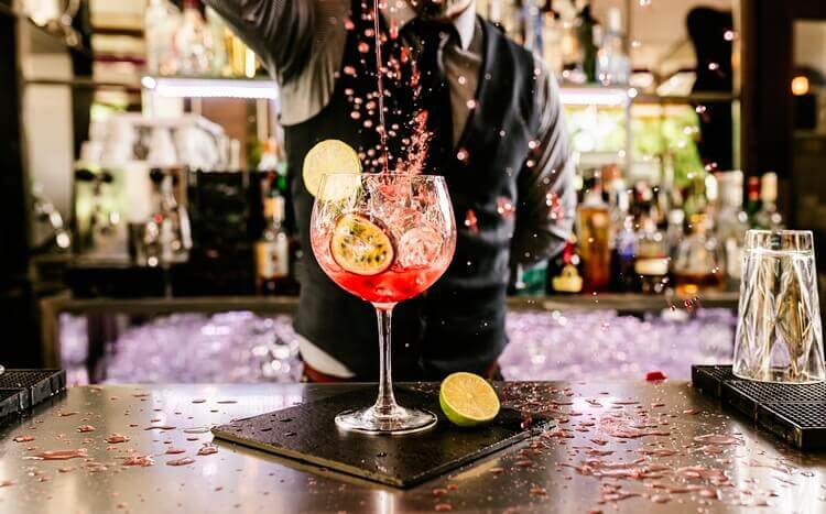 barman przygotowuje kolorowego drinka z limonką i marakują