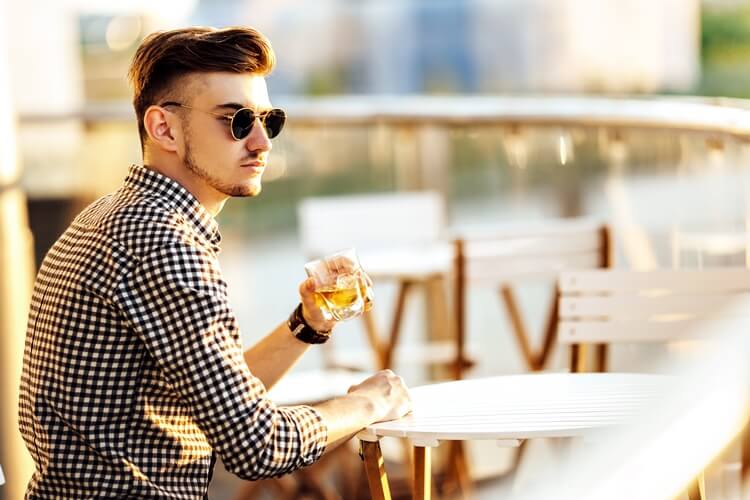 modny młody mężczyzna siedzi przy stoliku i pije whisky