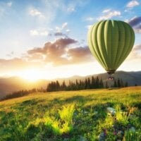 zielony balon na ogrzewane powietrze leci w górach na tle zachodu słońca