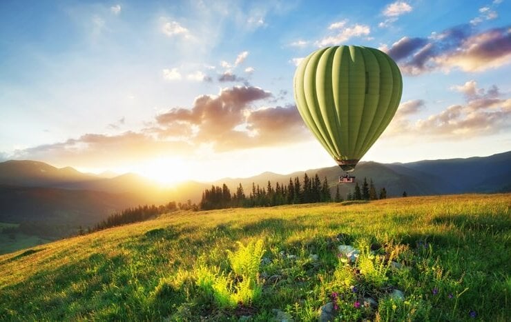 zielony balon na ogrzewane powietrze leci w górach na tle zachodu słońca