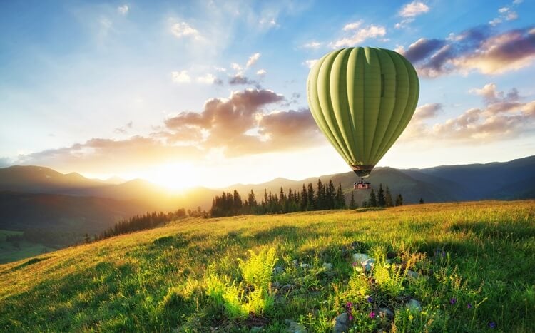 zielony balon na ogrzewane powietrze leci w górach na tle zachodu słońca