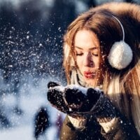 młoda kobieta zdmuchuje śnieg z wełnianych rękawiczek