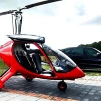 czerwony wiatrakowiec z zabudowaną kabiną pilota stoi na parkingu obok czarnego suva