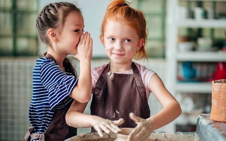 dwie dziewczynki na warsztatach ceramicznych szepczą sobie coś do ucha