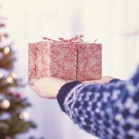 Kobieta trzymająca w rękach prezent na tle choinki świątecznej