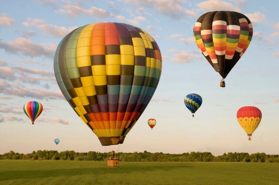 Balony lecące w powietrzu na tle nieba i lasu podczas wschodu słońca