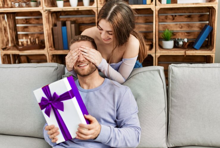 kobieta zakrywająca oczy mężczyźnie. Mężczyzna trzyma prezent