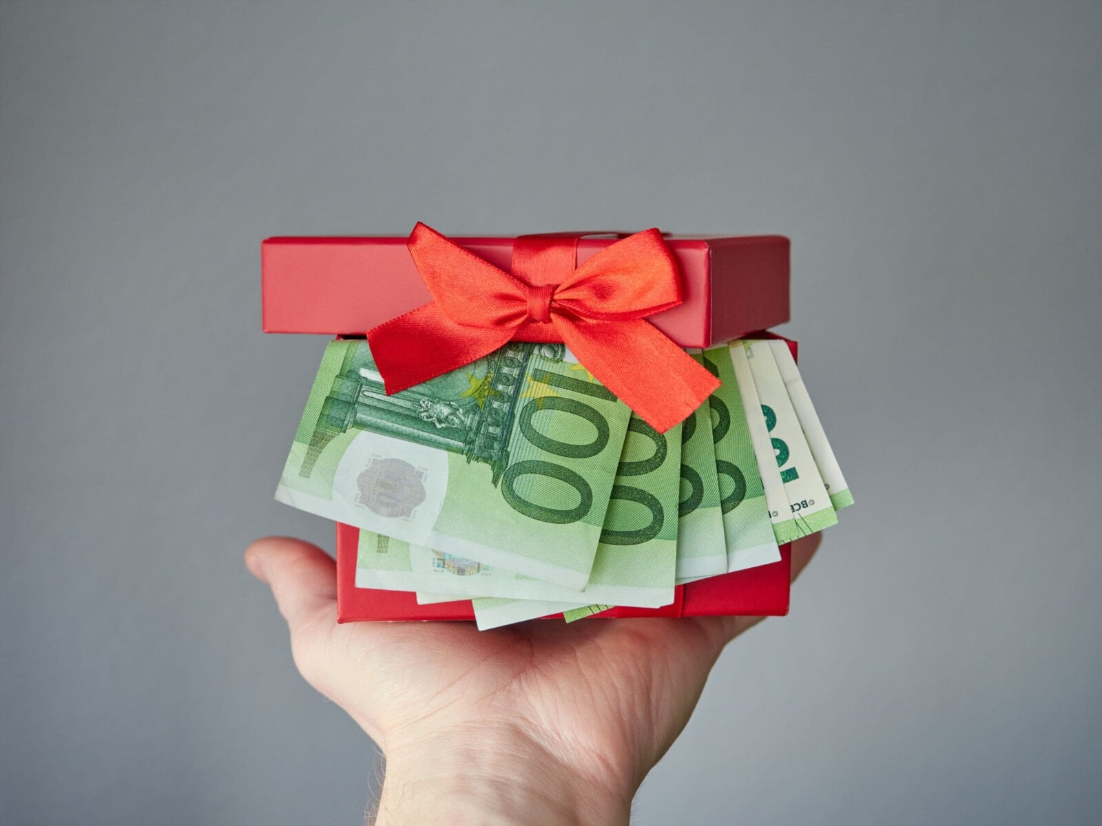 dłoń wręczająca prezent z banknotami wystającymi z pudełka