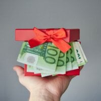 dłoń wręczająca prezent z banknotami wystającymi z pudełka