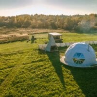 Widok z lotu ptaka na namioty glampingowe. Wokół las i zieleń.