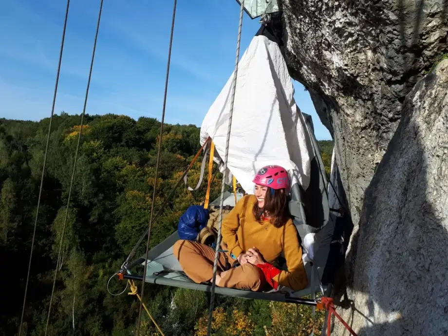 Kobieta w kasku przypięta linami leżąca na portaledge.
