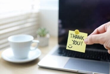 Dłoń trzymająca karteczkę z napisem "thank you" na tle laptopa