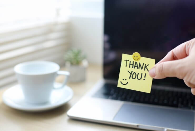 Dłoń trzymająca karteczkę z napisem "thank you" na tle laptopa