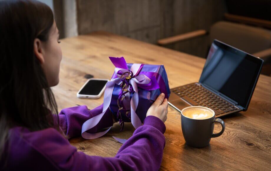 Fioletowy prezent leżący na stole, obok kawa i laptop