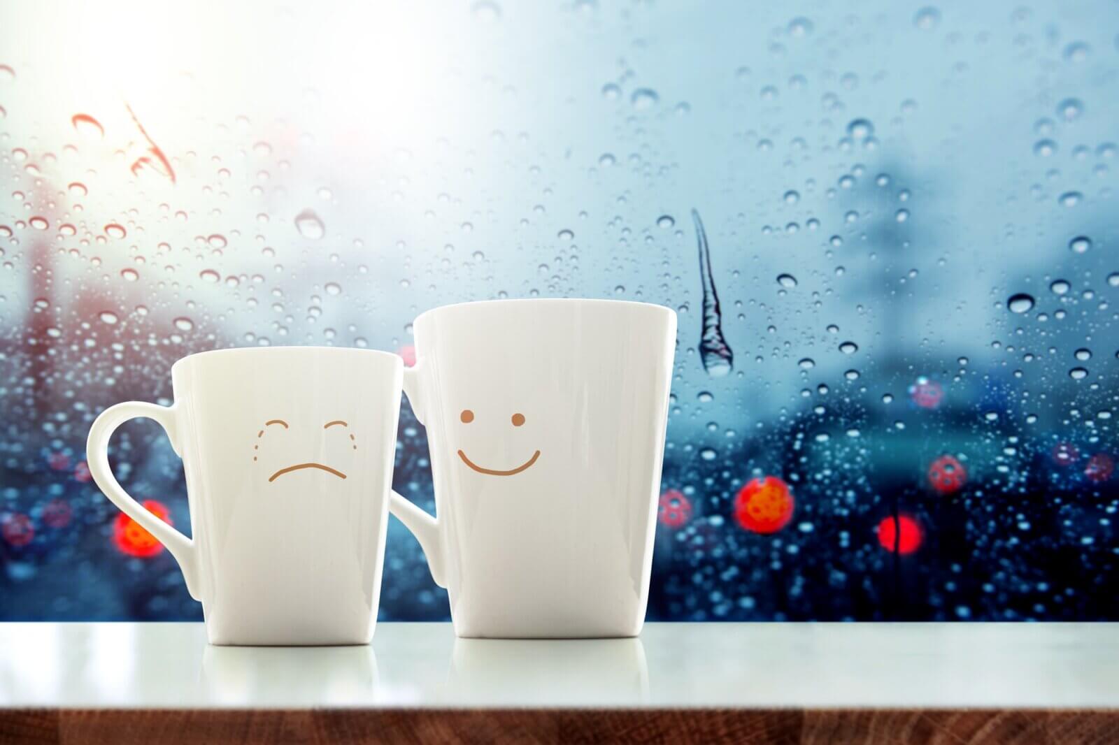 Dwa kubki z narysowanymi emocjami smutku i uśmiechu