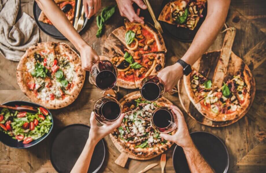 Ludzie stukają się kieliszkami z winem nad stołem z włoską pizzą
